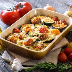 Eggplant And Zucchini Casserole on a wooden table with olive oil and other ingredients around dish