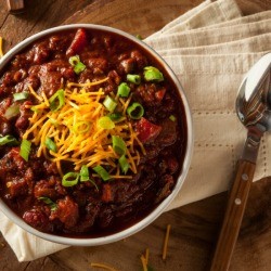 Chili with cheese and chives on wooden table
