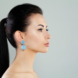 Profile of a woman with a pony tail and blue dangling earrings.