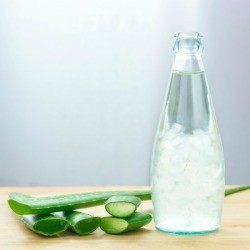 Bottle of aloe juice next to some cut aloe leaves.
