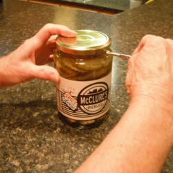A paint key being used to open a jar of pickles.