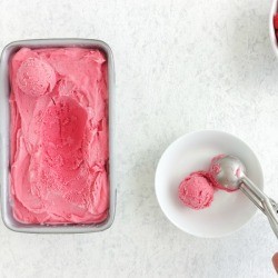Person scooping from a tub of ice cream next to a bowl of fresh raspberries.