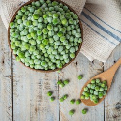 Frozen peans in a bowl with a wooden spoon on a weathered wood background.