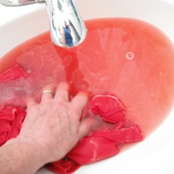 A red t-shirt that is being washed in the sink to remove the excess dye.