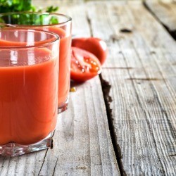 Two glasses of tomato juice on a rustic wood table.