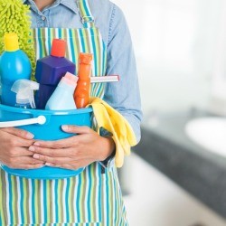 Person in an apron holding a bucket of cleaning supplies.