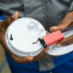 Man taking batteries out of a smoke detector.