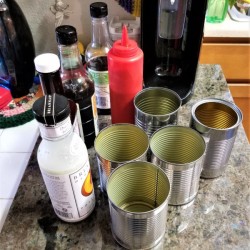A collection of recycled aluminum cans near tall narrow condiment bottles.