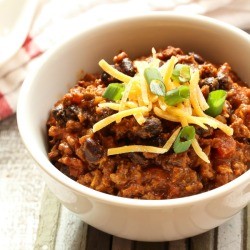 A bowl of chili with beans, topped with cheese and green onions.