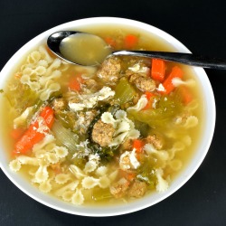 A bowl of Italian Wedding soup with meatballs, pasta, escarole and other veggies.