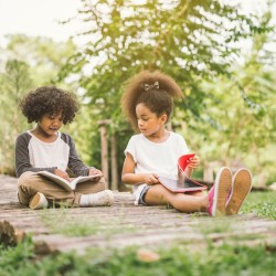 Two kids sitting on a rustic wooden bridge, reading books.